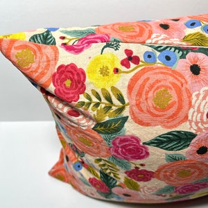 May include: A decorative pillow with a floral pattern. The pillow features large, colorful flowers in shades of pink, orange, yellow, and blue against a cream-colored background. Green leaves and stems are also visible.
