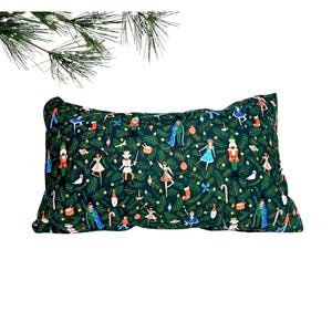 May include: Rectangular decorative pillow with a dark green background and a repeating pattern of Christmas-themed illustrations. The pattern includes nutcrackers, ballerinas, and other festive elements. The pillow is a rectangle shape.