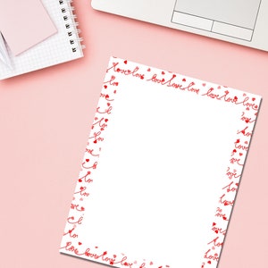 May include: A white sheet of paper with a red border of the word "love" and small hearts. The paper is on a pink surface, with a notebook, sticky notes, and a laptop visible in the background. The design is suitable for Valentine's Day or romantic occasions.