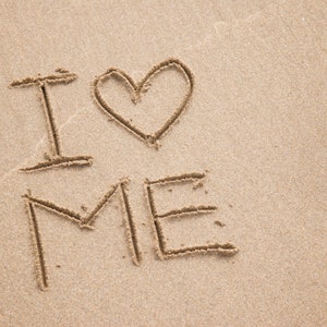 May include: The words "I love me" are written in the sand with a heart drawn between the words "I" and "me".