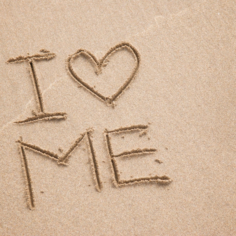 May include: The words "I love me" are written in the sand with a heart drawn between the words "I" and "me".