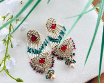 May include: A pair of gold earrings with red and green stones, white beads, and a pearl drop. The earrings are intricate and detailed, with a traditional Indian design.