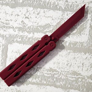 Puede incluir: Un cuchillo mariposa rojo con un patr&oacute;n de diamante en el mango.