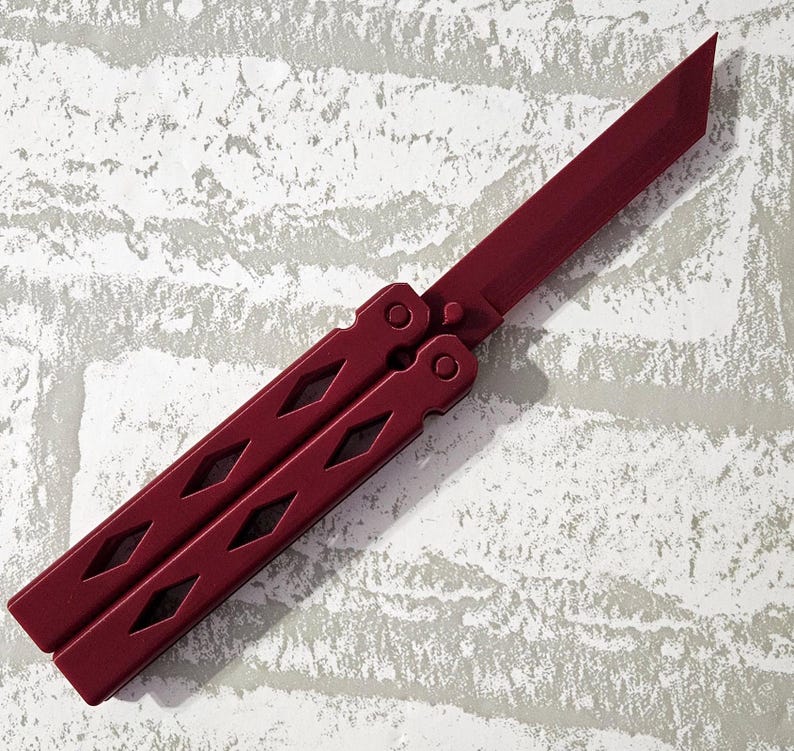 Puede incluir: Un cuchillo mariposa rojo con un patr&oacute;n de diamante en el mango.
