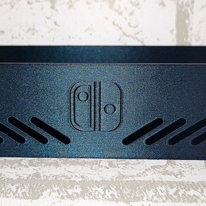 May include: A black plastic stand with a Nintendo Switch logo and ventilation slots. The stand is designed to hold a Nintendo Switch console.