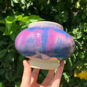 Könnte beinhalten: Ein Keramiktopf mit einem weißen Sockel und einer blauen, rosa und weißen Glasur. Die Glasur hat einen Marmoreffekt.