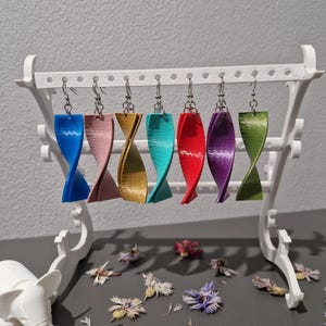 Può includere: Sei paia di orecchini pendenti colorati su un espositore bianco. Gli orecchini sono realizzati in plastica attorcigliata e sono disponibili in blu, rosa, oro, turchese, rosso e viola.