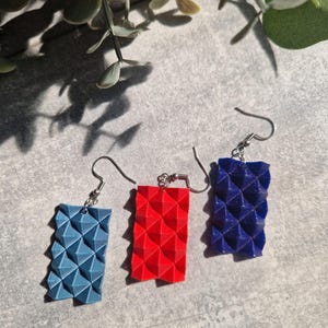 Può includere: Tre paia di orecchini geometrici con un design a forma di piramide. Gli orecchini sono blu, rossi e blu scuro.