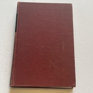 May include: A closed, hardcover book with a textured, maroon cover. The book's spine is visible on the left side, and the pages are bound tightly together. The cover shows some signs of wear.