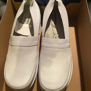 May include: A pair of white Easy Works slip-on shoes, featuring a rounded toe and elastic band across the top. The shoes are in a cardboard box. The brand name and features are visible on the insole.