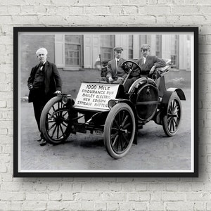 May include: A black and white photo of a Bailey Electric car with a sign that reads "1000 Mile Endurance Run Bailey Electric New Edison Storage Batter". Three men are standing near the car.