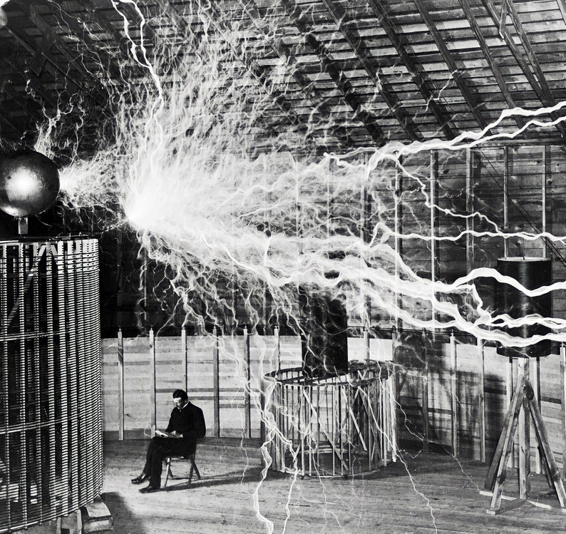 May include: Black and white photograph of a man seated, reading, amidst a display of electrical arcs. A large spherical object and a cylindrical structure are visible, with lightning-like energy emanating from them. The scene is set in a wooden-framed building.