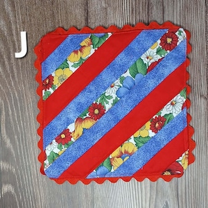 May include: Square quilted hot pad with a red scalloped edge. The design features diagonal red stripes alternating with blue stripes patterned with colorful flowers. The hot pad is likely handmade and suitable for kitchen use.