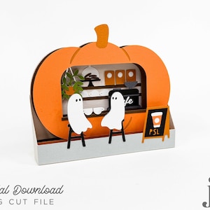 May include: A Halloween-themed papercraft scene featuring a pumpkin-shaped cafe. Two white ghost figures sit at a counter. The cafe has a coffee sign that says "PSL". The words "Digital Download SVG Cut File" are also visible.