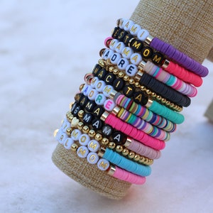 Pode incluir: Uma pilha de pulseiras de contas coloridas com diferentes palavras escritas nelas, incluindo "Mami", "Mom", "Grandma" e "Girl".