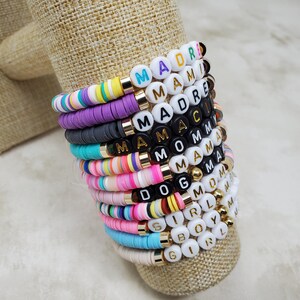 Pode incluir: Uma pilha de pulseiras de contas coloridas com diferentes palavras escritas nelas, incluindo "Mama", "Mom", "Girl" e "Boy".