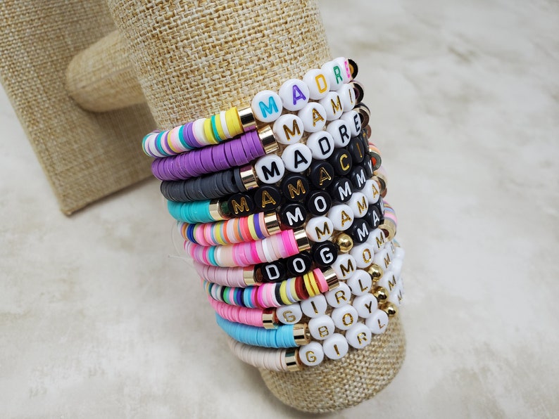 Pode incluir: Uma pilha de pulseiras de contas coloridas com diferentes palavras escritas nelas, incluindo "Mama", "Mom", "Girl" e "Boy".
