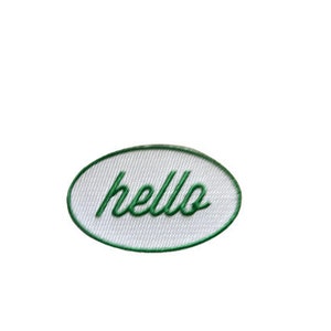 May include: White oval-shaped patch with a green embroidered outline and the word "hello" in green cursive lettering.