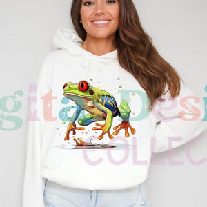 Puede incluir: Sudadera con capucha blanca con un gráfico de rana colorido. La rana es verde, azul, amarilla y roja con ojos negros. La rana está sentada en una rama con gotas de agua a su alrededor.
