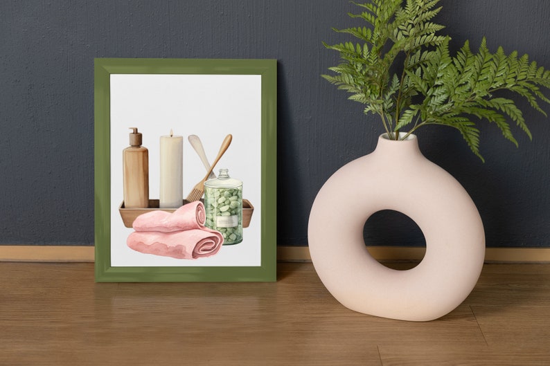 Op de afbeelding: Een ingelijste illustratie van spa-artikelen, waaronder een kaars, zeep, handdoeken en een pot badzout. De illustratie is in een groene lijst en ligt op een houten oppervlak.