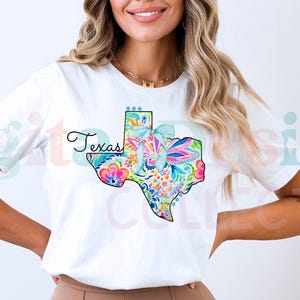 Może przedstawiać: Biała koszulka z kolorowym kwiatowym wzorem przedstawiającym stan Teksas i napisem "Texas" nadrukowanym z przodu.