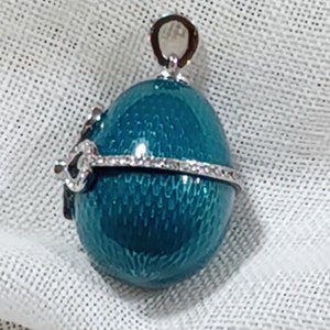 Puede incluir: Pendiente en forma de huevo azul turquesa con una banda plateada de diamantes de imitaci&oacute;n alrededor del centro. El pendiente tiene un bucle plateado en la parte superior para sujetar una cadena.