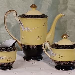 May include: A vintage tea set with a yellow and black design. The set includes a teapot, creamer, and sugar bowl. Each piece features a dragon motif and gold accents. The teapot has a tall, slender spout and a matching lid.