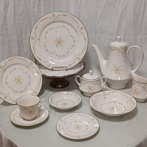 May include: A complete white porcelain tea set with a floral pattern. The set includes plates, bowls, a teapot, a creamer, a sugar bowl, and a teacup with a saucer. Each piece has a green trim and a yellow floral design.