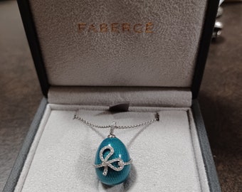 Puede incluir: Un collar con un colgante en forma de huevo Fabergé azul turquesa adornado con un lazo engastado con diamantes. El collar se presenta en una caja de terciopelo blanco con el logotipo de Fabergé.