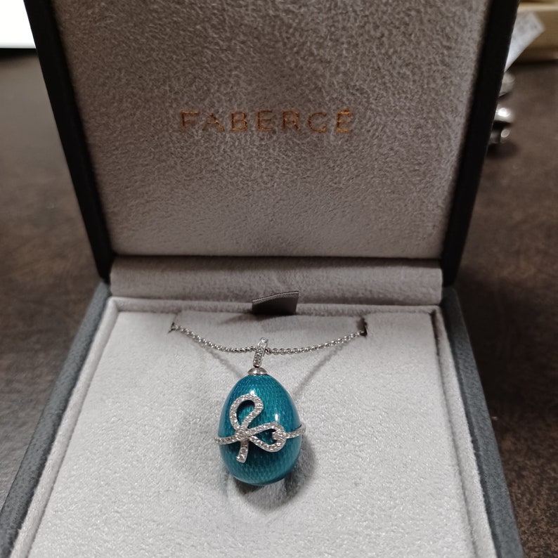 Puede incluir: Un collar con un colgante en forma de huevo Faberg&eacute; azul turquesa adornado con un lazo engastado con diamantes. El collar se presenta en una caja de terciopelo blanco con el logotipo de Faberg&eacute;.