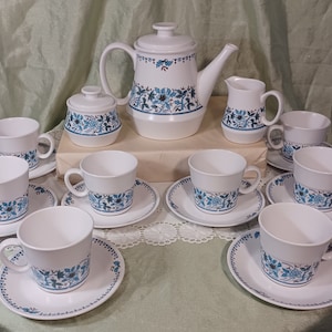 May include: A white ceramic tea set with a blue floral design. The set includes a teapot, sugar bowl, creamer, and multiple cups and saucers. The floral pattern is repeated on each piece, creating a cohesive and elegant look.