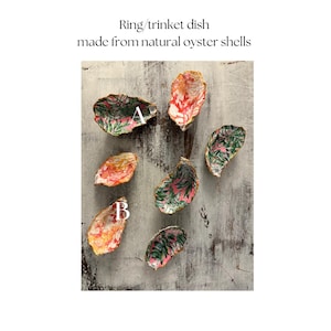 May include: Seven small decorative dishes made from natural oyster shells. The dishes are lined with colorful floral patterned paper. The dishes are arranged on a light gray wooden surface.