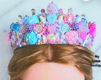 Könnte beinhalten: Eine dekorative Krone mit einer bunten Auswahl an Miniatur-Süßigkeiten-Verzierungen, darunter Lutscher, Donuts, Spiralen und Perlen in Rosa-, Blau- und Violetttönen. Der Text My Sweets Boutique ist unten rechts auf dem Bild zu sehen.
