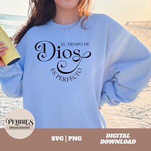 May include: A light blue sweatshirt with the text "El tiempo de Dios es perfecto" in black cursive lettering. The text is centered on the sweatshirt.