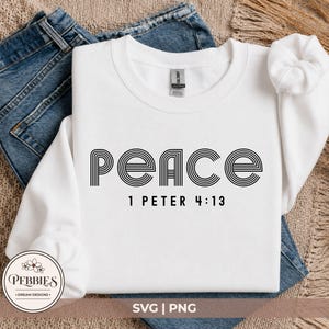 May include: A white long-sleeve crewneck sweatshirt featuring the word "peace" in a black, multi-line retro font, with the text "1 PETER 4:13" printed in a simple black sans-serif typeface directly underneath the main word.