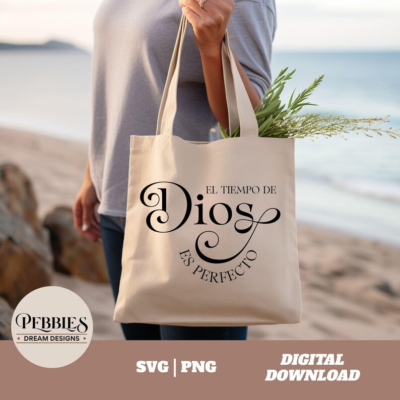 May include: A white tote bag with black text that reads "El Tiempo de Dios es Perfecto". The bag is being held by a person on a beach.