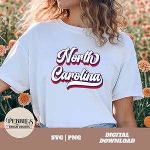 Puede incluir: Camiseta blanca con un gráfico retro de color rojo, blanco y azul que dice "North Carolina".