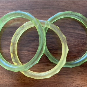 Puede incluir: Tres anillos de vidrio verde, cada uno con una forma y un tamaño ligeramente diferentes, están apilados uno encima del otro.