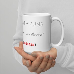 Könnte beinhalten: Weiße Keramiktasse mit schwarzem Text, der "Math Puns: You are the first sign of (madness)" lautet.