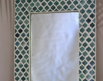May include: A green and white decorative mirror with a geometric pattern. The mirror has a rectangular shape and a white frame.