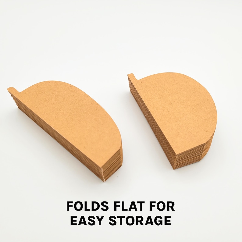 May include: Two stacks of brown, semi-circular paper coffee filters. The filters have a small tab on one side. Text at the bottom reads "FOLDS FLAT FOR EASY STORAGE".