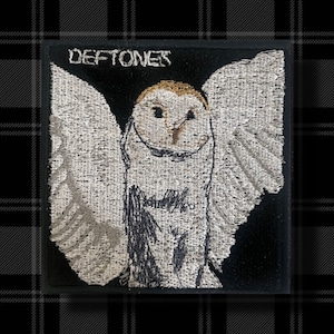 May include: Embroidered patch with a white owl design and the word "Deftones" above it, set against a black square. The owl has outstretched wings. The patch is textured, suitable for clothing or accessories.