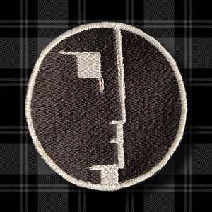 May include: A black and white embroidered patch featuring a stylized portrait of a person. The patch is circular and has a white border.