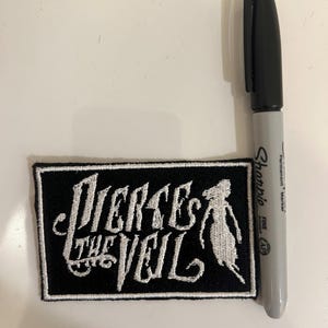 May include: Black and white embroidered patch with the text "Pierce the Veil" in a stylized font. A white silhouette of a person is to the right of the text.
