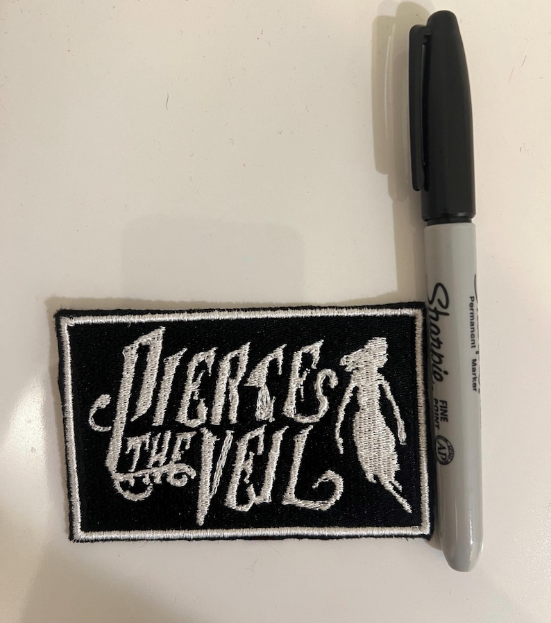 May include: Black and white embroidered patch with the text "Pierce the Veil" in a stylized font. A white silhouette of a person is to the right of the text.