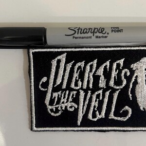 May include: Black and white embroidered patch with the text "Pierce the Veil" in a stylized font. The patch features a white silhouette of a person with long hair.