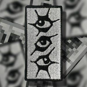 May include: A rectangular patch with a black border and a gray background. The patch features three stylized black eye designs stacked vertically. The eyes have a unique, abstract appearance, with pointed extensions emanating from the eye shape.