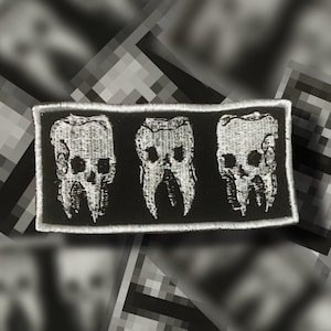 May include: Embroidered patch featuring three stylized teeth with skull-like features. The teeth are white with black detailing, set against a black rectangular background with a white border. The patch has a gothic or alternative aesthetic.