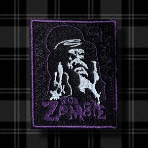 May include: A black and purple embroidered patch with a white silhouette of a zombie with the word "Zombie" written in purple below it.