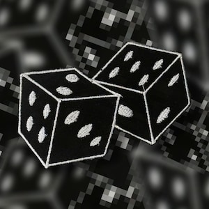 May include: Two black dice patches with white embroidered pips. The dice are embroidered with a white outline. The background is a blurred, pixelated pattern in black and white.